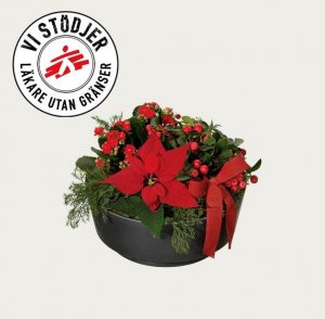 Låg, rund julgrupp med röd julstjärna, röd våreld, vaktelbär och gran/tall. Plus en röd rosett. Skicka julgruppen med ett bud från Interflora!