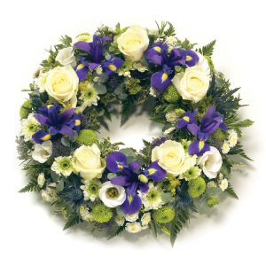 Begravningskrans "En sista hälsning", med blommor i blått, vitt och lime på en bädd av gröna blad. Kransen är öppen i mitten. Du hittar den i Euroflorists webbutik.
