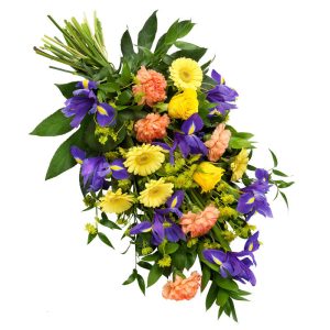 Färgstark, liggande sorgbukett, med blandade snittblommor i blått, gult och aprikost plus gröna blad.