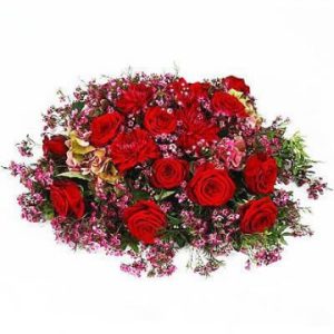 Oerhört vacker, låg begravningsdekoration, med blommor i rött och lila och små gröna blad. Arrangemanget finns att beställa i olika storlekar.