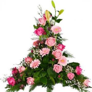 Hög begravningsdekoration, med rosa snittblommor mot en bas av gröna blad. Här: rosa rosor, rosa gerberas, rosa liljor (blomsorter kan variera något beroende på tillgång i den butik som får hand om ditt blomsterbud).